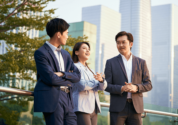 Three business professionals having a casual conversation outdoors in a modern urban setting with skyscrapers in the background.